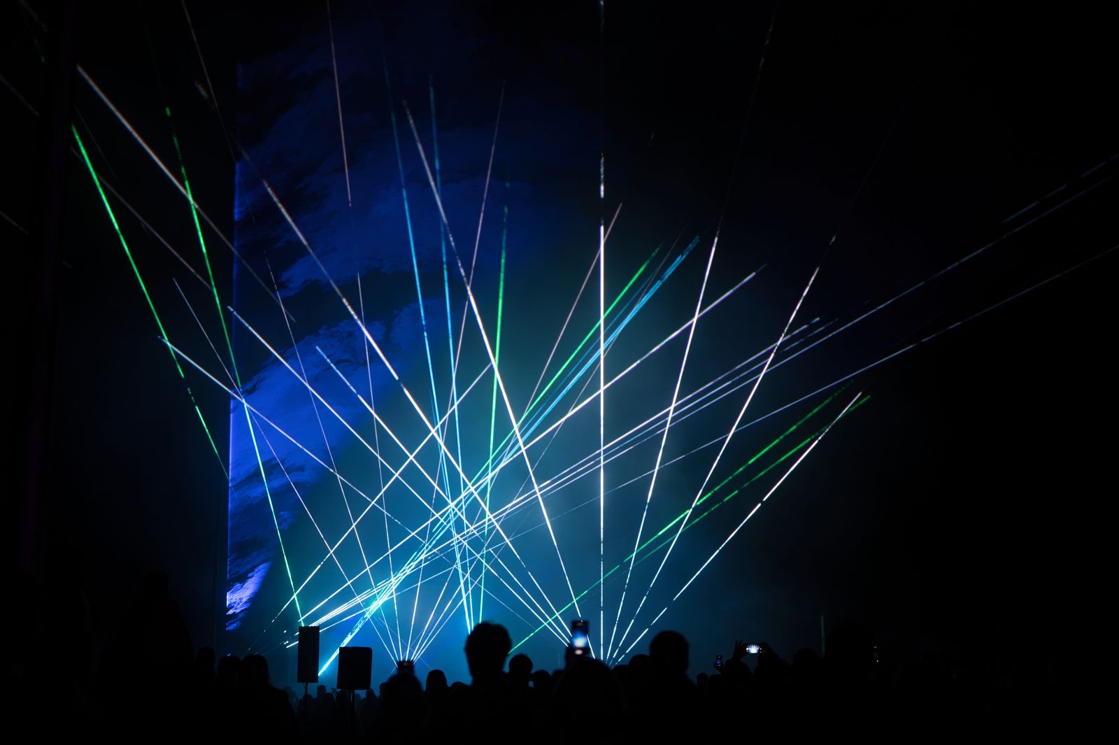 Green and blue laser beams fanning out over a crowd at a night event